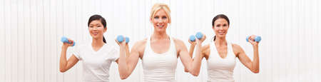 Panorama web banner interracial group of three beautiful young women sitting practising pilates with weights at a gymの写真素材