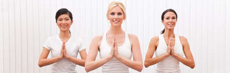 Panoramic web banner interracial group of three beautiful young women hands in prayer practising yoga at a gym or health clubの写真素材