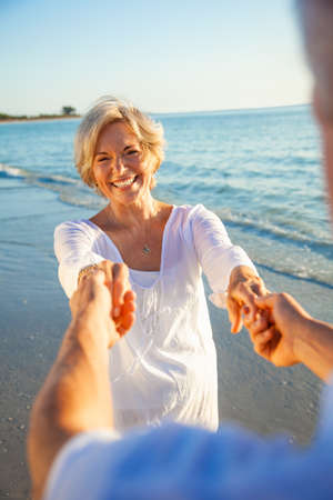 Happy senior man and woman couple dancing and holding hands on a deserted tropical beach at sunset with bright clear blue skyの写真素材