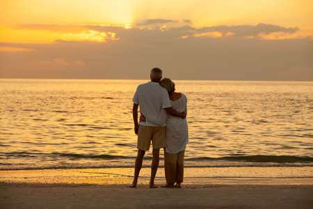Senior man and woman couple embracing at sunset or sunrise on a deserted tropical beachの写真素材