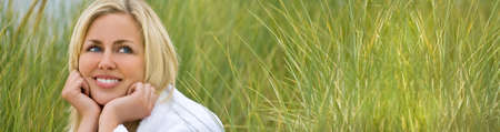 Panoramic web banner blonde girl young woman wearing a white towelling robe sitting in tall natural green grassの写真素材