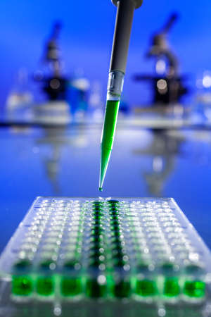 Environmental concept in a medical research laboratory or lab showing samples of a green solution with a pipette, ninety six well cell tray and microscopesの写真素材
