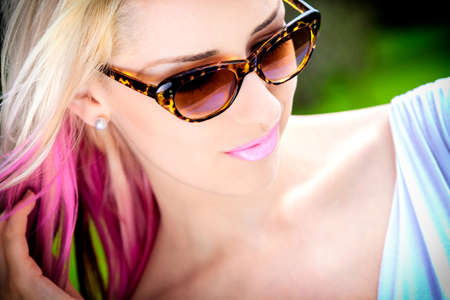 Outdoor portrait of a beautiful young woman or girl with blond and pink hair wearing sunglasses outsideの写真素材