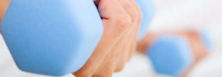 Close up panorama web banner of young woman or girl female hands exercising lifting blue weights at a gymの写真素材