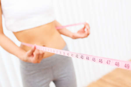 Young woman girl female measuring her waist or waistline with a pink tape measureの写真素材