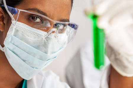 Female Indian Asian woman scientist or doctor looking at a test tube of a green solution in a medical research lab or laboratoryの写真素材