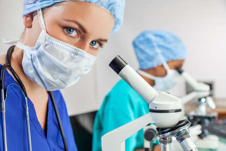 Female medical or scientist using a microscope in a research lab or laboratory with her colleagueの写真素材
