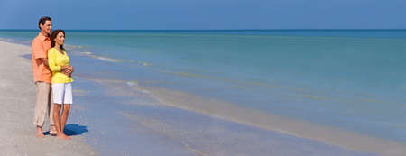 Man and woman romantic couple in standing on a deserted tropical beach with bright clear blue sky panorama web bannerの写真素材