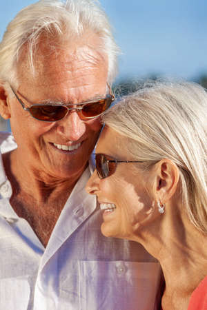 Happy senior loving man and woman romantic couple together outside in sunshine laughing wearing sunglassesの写真素材