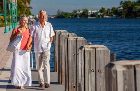 Happy senior man and woman romantic couple together looking out to tropical sea or river with bright clear blue skyの写真素材