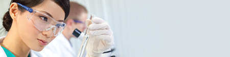 Chinese Asian woman female medical scientist, scientific researcher or doctor looking at a test tube of clear liquid in a medical research lab or laboratory with her behind her. Panoramic web banner panoramaの写真素材