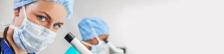 Female medical or scientist using a microscope in a research lab or laboratory with her colleagueの写真素材