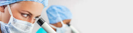 Panoramic web banner female medical or scientist using a microscope in a research lab or laboratory with her colleague panoramaの写真素材