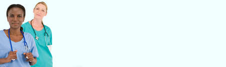 Female African American doctor or nurse with her caucasian colleague behind her wearing scrubs and stethoscopes in hospital panoramic web banner. Mixed race medical team panorama.の写真素材