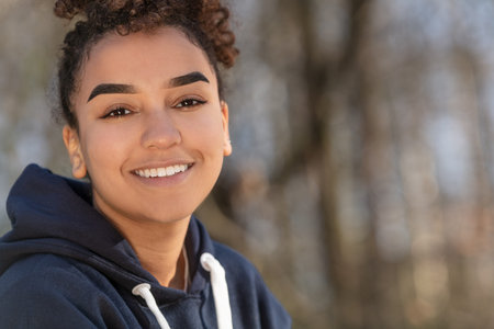 Outdoor portrait of beautiful happy mixed race biracial African American girl teenager female young woman smiling with perfect teeth wearing a blue hoodieの写真素材