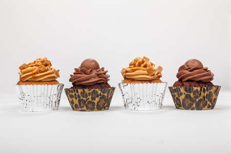 Four cup cakes with icing or frosting, two chocolate and two caramel, photographed on a white backgroundの写真素材