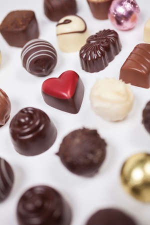 Handmade chocolates or candies including a romantic heart shaped red one photographed from above on a white backgroundの写真素材
