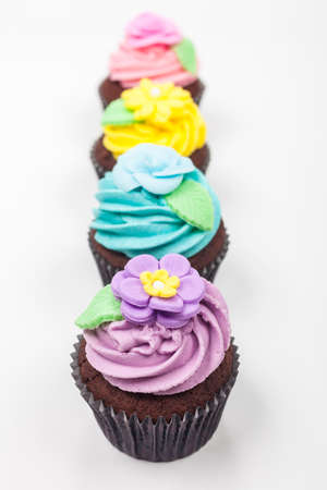 Four chocolate cup cakes with icing or frosting, pink, purple, blue and yellow with green leaves, photographed on a white backgroundの写真素材