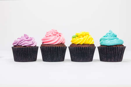 Four chocolate cup cakes with icing or frosting, pink, purple, blue and yellow with green leaf, photographed on a white backgroundの写真素材