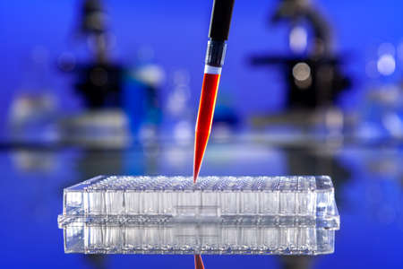 Laboratory blood test or lab testing samples of blood or a red solution with a pipette, ninty six well cell tray and microscopesの写真素材