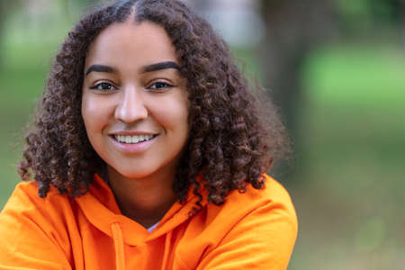 Outdoor portrait of beautiful happy mixed race biracial African American girl teenager female young woman smiling with perfect teeth and wearing an orange hoodieの写真素材