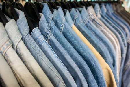 Male mens denim jeans shirts sorted on clothes hangers on a shop wardrobe closet railの写真素材
