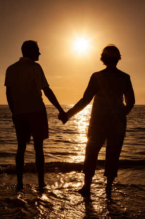Senior man and woman couple holding hands at sunset or sunrise on a deserted tropical beachの写真素材