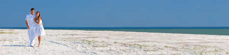 Panorama man and woman romantic couple on vacation in white clothes walking and laughing together on a deserted tropical beach with blue sky. Panoramic web banner.の写真素材