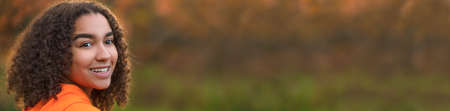 Panorama beautiful happy mixed race African American girl teenager female young woman smiling with perfect white teeth outdoors in Fall or Autumn panoramic web banner.の写真素材