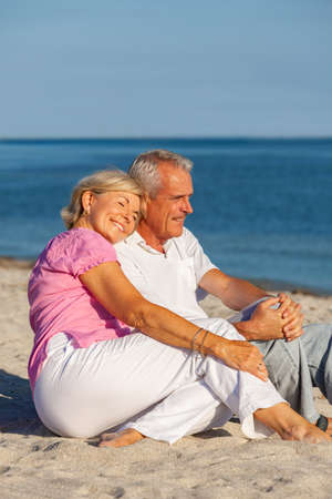 Happy senior man and woman couple sitting together on a deserted tropical beach with bright clear blue skyの写真素材