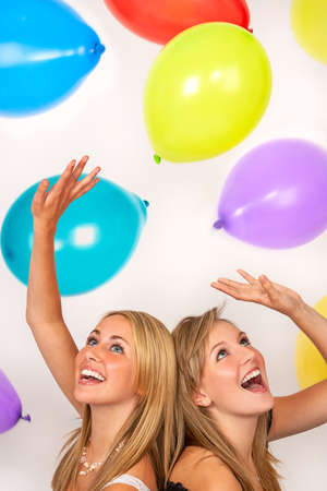Two beautiful happy teenage girls, female young women, celebrating or at a party with colorful balloonsの写真素材