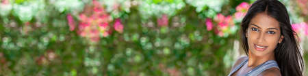 Panorama outdoor portrait of a beautiful Asian Indian girl or young woman surrounded by flowers. Panoramic web banner.の写真素材