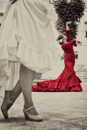 Sepia toned photograph of women traditional Spanish Flamenco dancers dancing in a town square, the focus is on the dancer in the red dressの写真素材