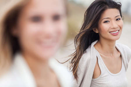 Outdoor profile portrait of a beautiful smiling happy Chinese Asian young woman or girl with blond female friend at beachの写真素材