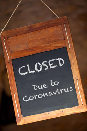 Traditional wooden blackboard or chalkboard sign hanging in a window saying Closed Due to Coronavirusの写真素材