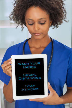 Black African American female medical doctor in a hospital with Coronavirus COVID-19 social distancing advice on a tablet computerの写真素材