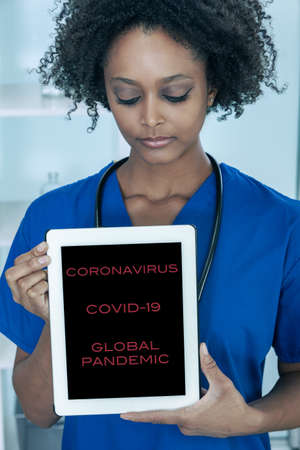 Black African American female medical doctor in a hospital holding a tablet computer with Coronavirus COVID-19 Pandemic Textの写真素材