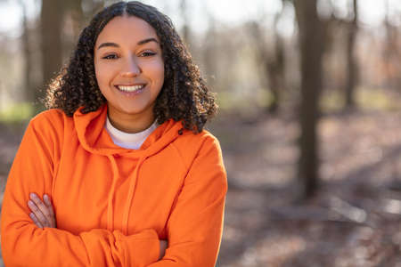 Outdoor portrait of beautiful happy mixed race biracial African American girl teenager female young woman arms folded laughing and smiling with perfect teeth in golden evening sunshine  の写真素材