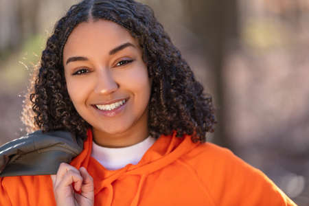 Outdoor portrait of beautiful happy mixed race biracial African American girl teenager female young woman laughing and smiling with perfect teeth in golden evening sunshine  の写真素材