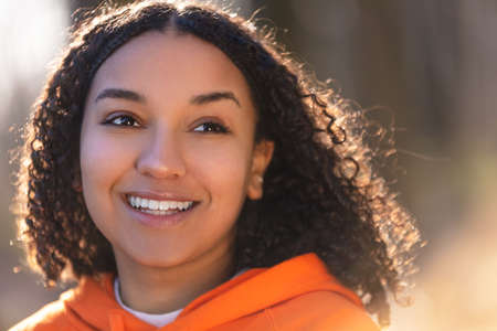 Outdoor portrait of beautiful happy mixed race biracial African American girl teenager female young woman smiling with perfect teeth wearing an orange hoodieの写真素材