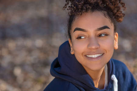 Outdoor portrait of beautiful happy mixed race biracial African American girl teenager female young woman smiling with perfect teeth wearing a blue hoodieの写真素材