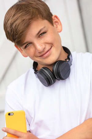 Boy teenager teen male child outside using his mobile cell phone and wireless headphones for social mediaの写真素材
