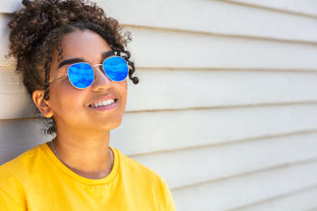 Girl teenager teen mixed race biracial African American female young woman wearing blue sunglasses smiling with perfect teeth on vacation in summer sunshineの写真素材