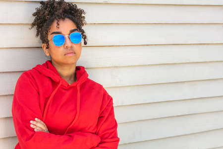 Girl teenager cool teen mixed race biracial African American female young woman wearing blue sunglasses and a red hoodie on vacation in summer sunshineの写真素材