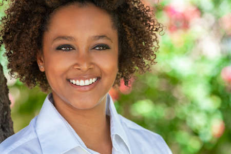 Beautiful young mixed race black African American woman with perfect teeth smiling and relaxing outside in summer sunshineの写真素材