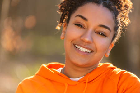 Outdoor portrait of beautiful happy mixed race biracial African American girl teenager female young woman laughing and smiling with perfect teeth in golden evening sunshineの写真素材