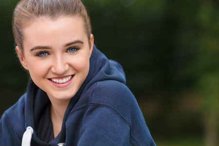 Beautiful girl teenager female young woman with blue eyes outside wearing dark blue hoodie happy and...