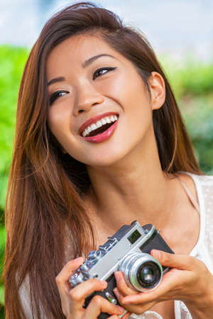 Beautiful Asian Chinese girl or young woman photographer outside laughing with perfect teeth taking pictures or photographs with a retro style cameraの写真素材