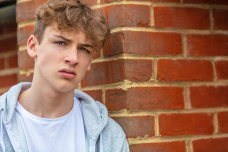 Serious male boy teenager outside leaning on brick wall wearing a gray hoody in urban cityの写真素材