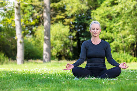Mature middle aged fit healthy woman practicing yoga outsidein a natural tranquil green environmentの写真素材
